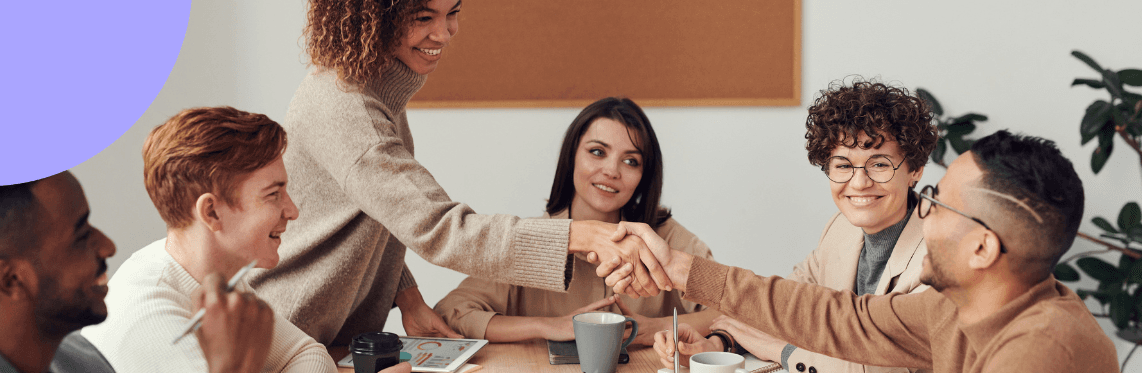 A group of employees gathered around a table shaking hands.
