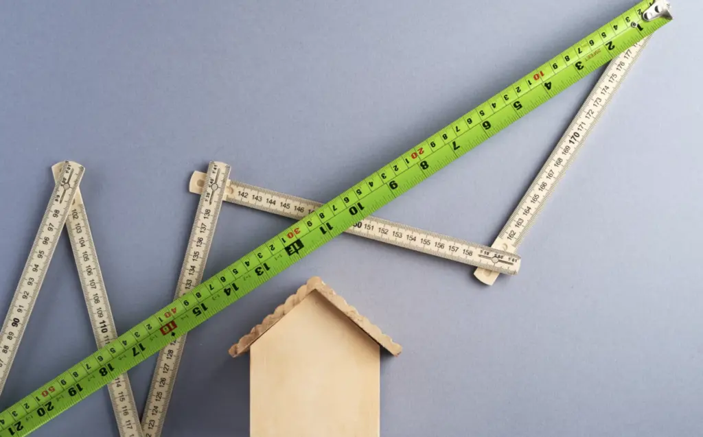 An image of green measuring tape and a multi-angled ruler over a small wooden birdhouse.