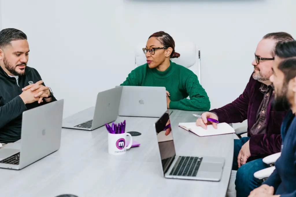 A group of employees sitting at a table with computers open in an ERG budget discussion. 