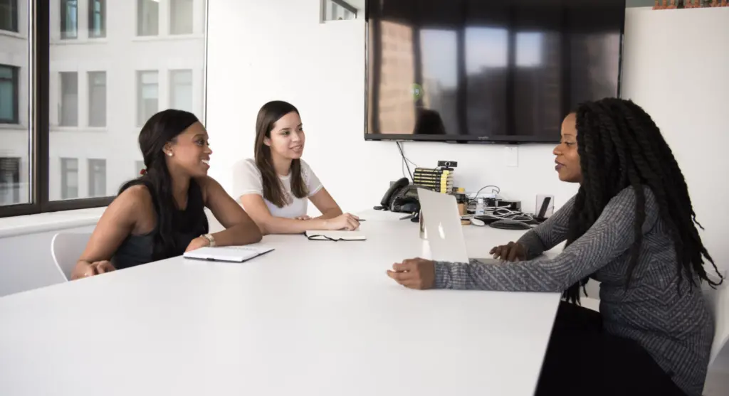 Three women sitting at a table in an office with notebooks and computer open, discussing ERG growth. 