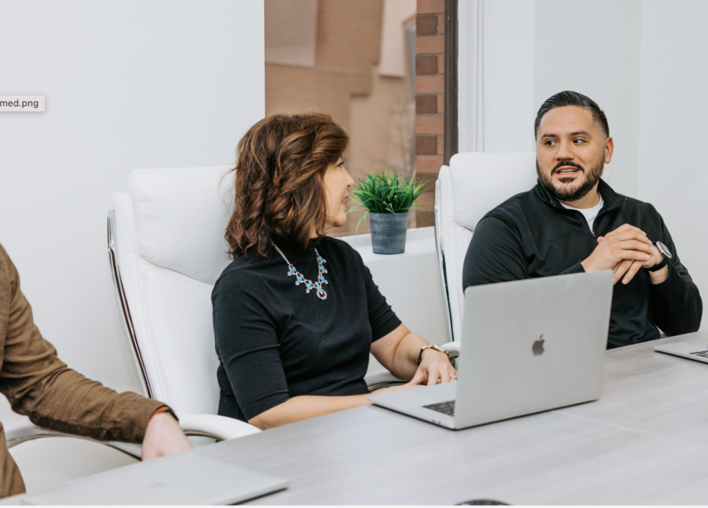 Two employees sitting in an diverse workplace setting having a conversation. 